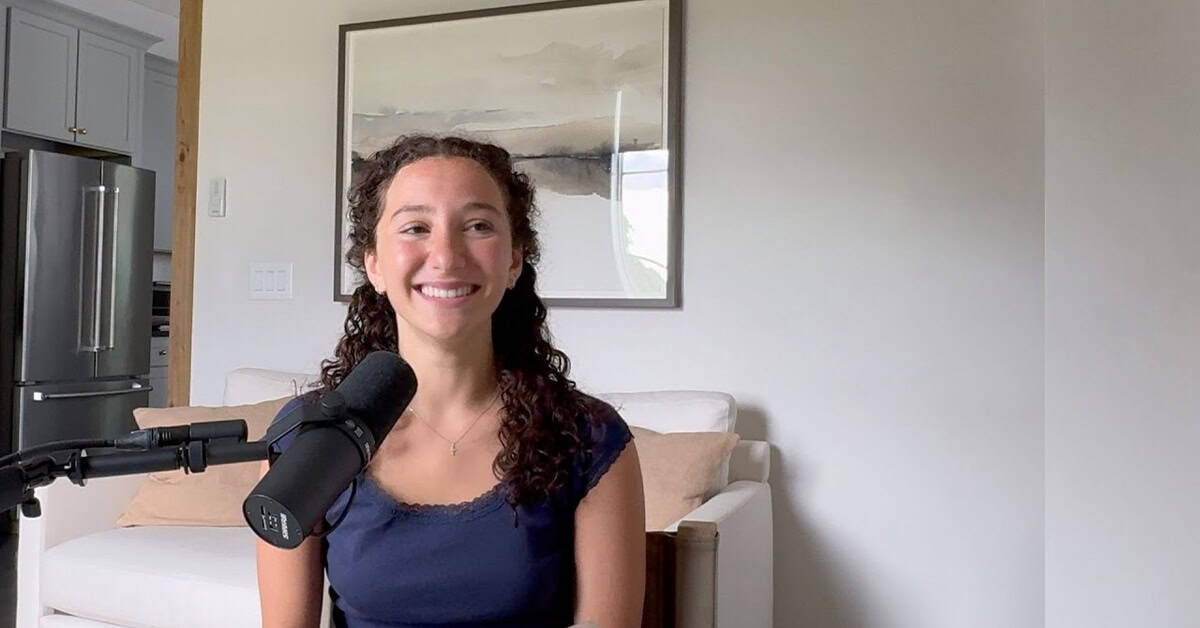 Young woman with curly hair smiling in front of microphone for America Out Loud News, podcast recording, outspoken news commentary, vibrant personality and engaging discussion.