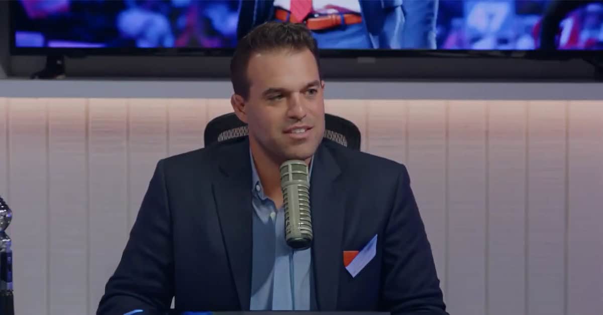 Charlie Kirk’s producer Andrew Kolvet Podcast host speaking into a microphone in a recording studio, with America Out Loud News branding in the background.