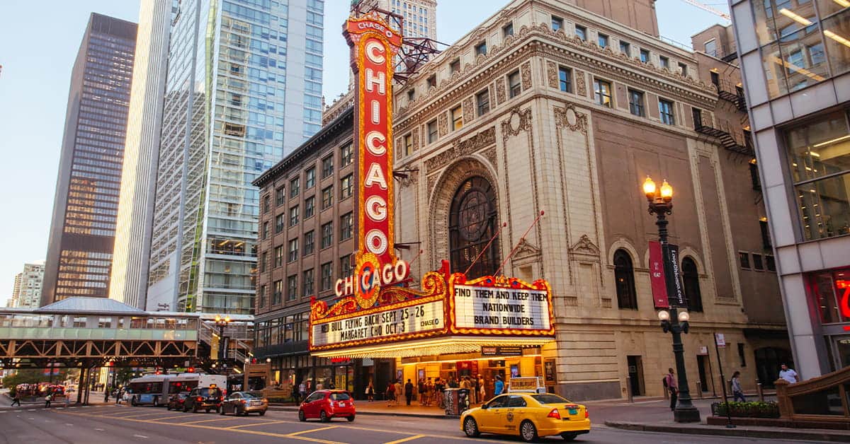Chicago Theatre marquee in downtown Chicago, Illinois, surrounded by skyscrapers, featuring vibrant lighting and advertising, representing iconic American entertainment and news hub.