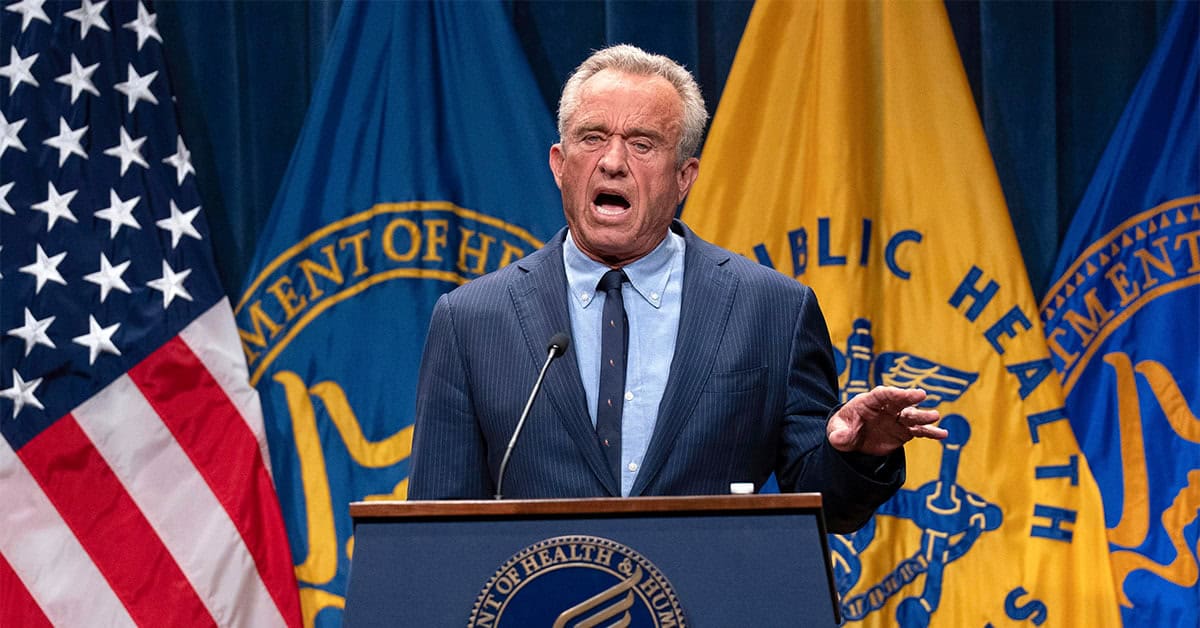 Man speaking passionately at a health department event with U.S. flags and health agency banners in the background, emphasizing public health and government leadership.