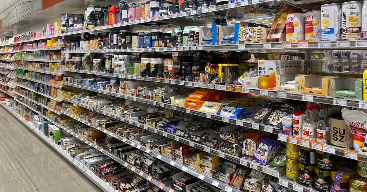 Assorted nutritional supplements and energy bars on grocery store shelves for health-conscious consumers.