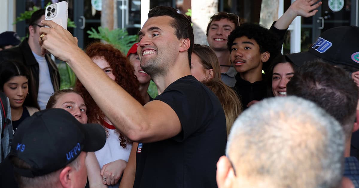 Portrait of a man taking a selfie with a diverse group of excited young people outside, illustrating community engagement and positive social interactions for America Out Loud News.