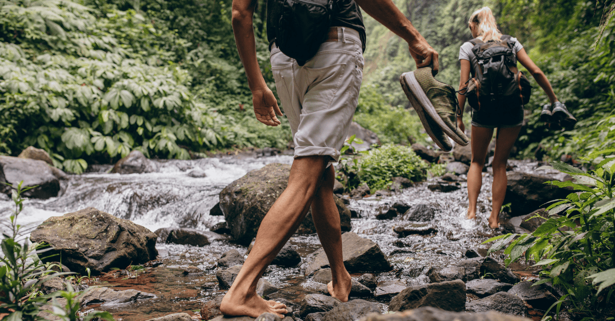 Earth-toned hiking shoes, backpack, footprints, forest, water, nature, adventure, outdoor activity, exploration, wilderness, trail, river, greenery, trekking, travel, trekking gear, outdoor exploration, scenic, nature photography, adventure travel.