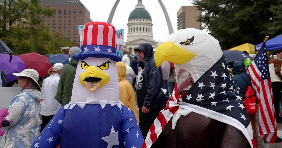Demonstrators wearing inflatable bald eagle costumes gather in Kiener Plaza during the “No Kings” protest in St. Louis, with the Gateway Arch in the background