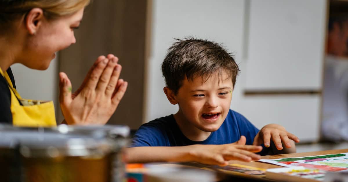 The teacher claps her hands and rejoices at the small victory of her student boy with down syndrome at painting studio for special need children. Development of children with spesial needs.