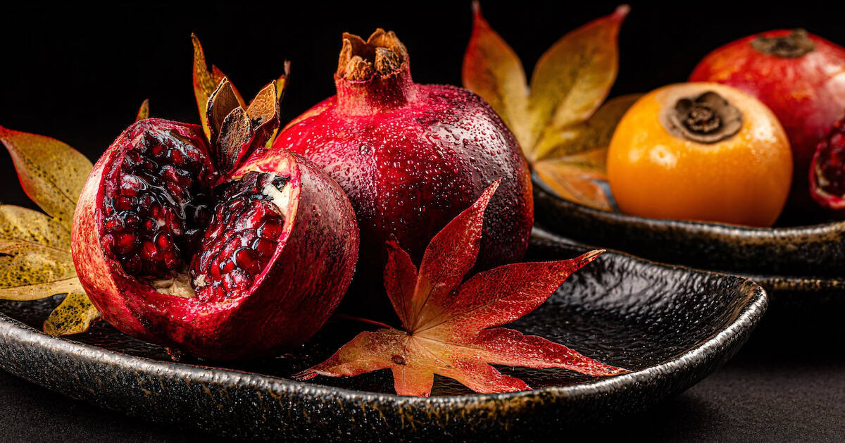 Tabletop arrangement of pomegranates, persimmons, and autumn leaves on ceramic plates