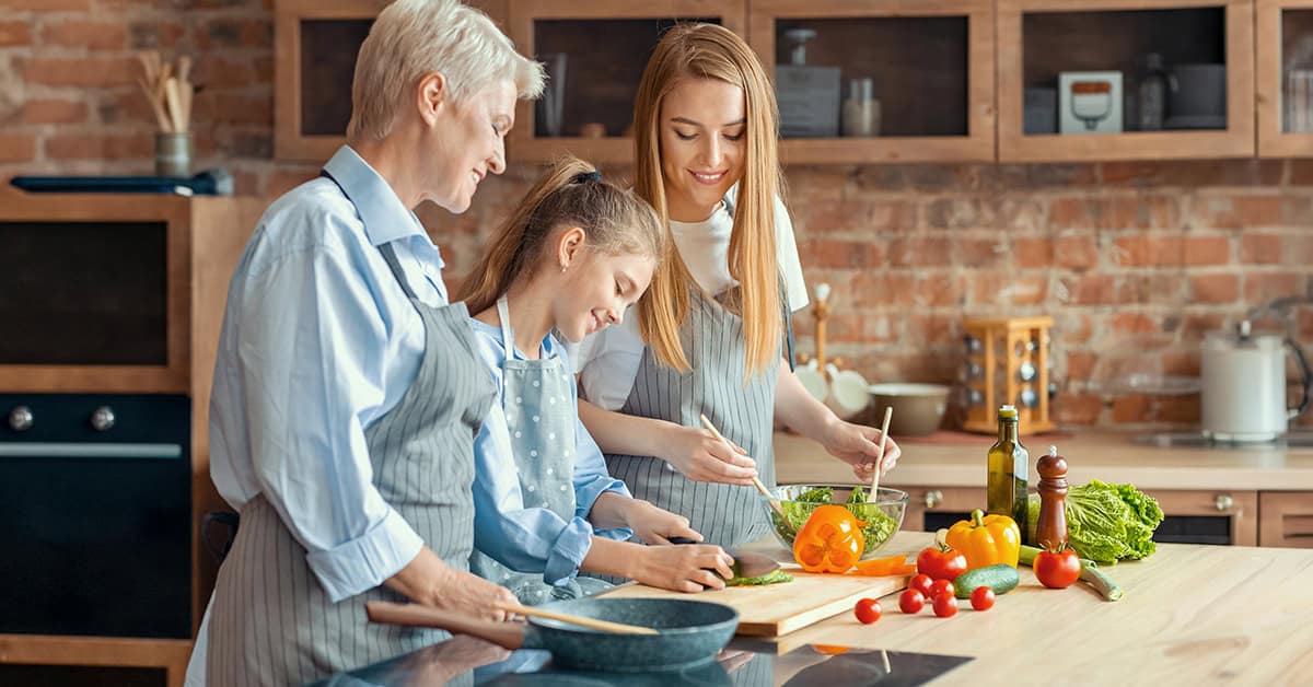 Happy adult ladies teaching little girl how to cook healthy food