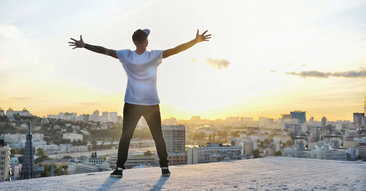 man with open arms facing a city’s silhouette at the sunset