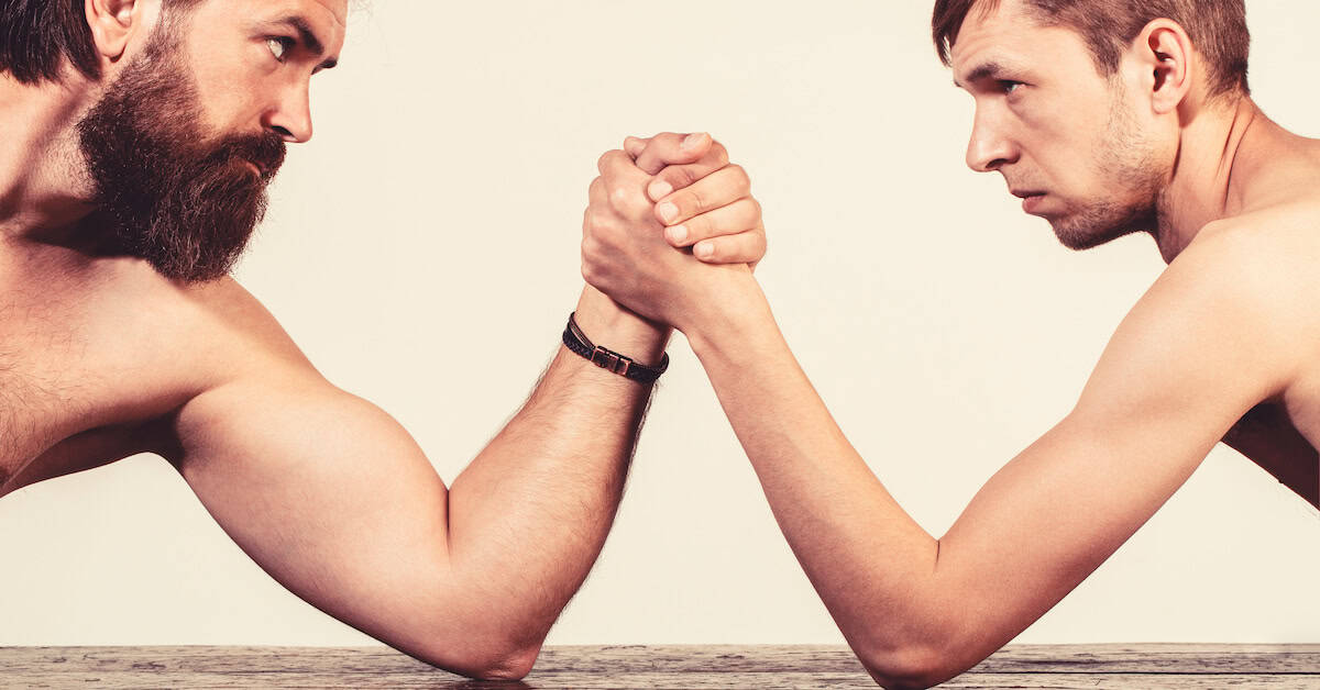 Heavily muscled bearded man arm wrestling a puny weak man